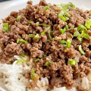 A white plate with rice and ground beef with teriyaki. Chopsticks in the background.