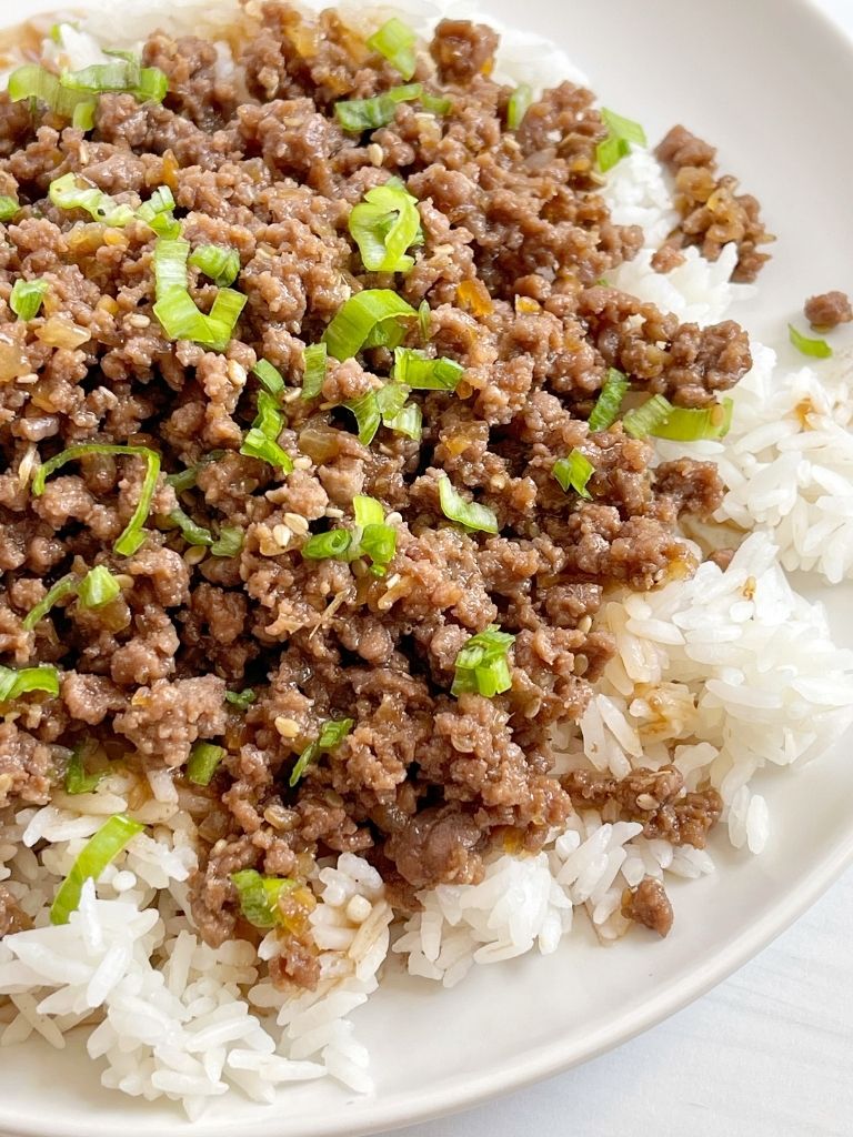 A white plate of white rice and ground beef teriyaki. Garnished with green onions.