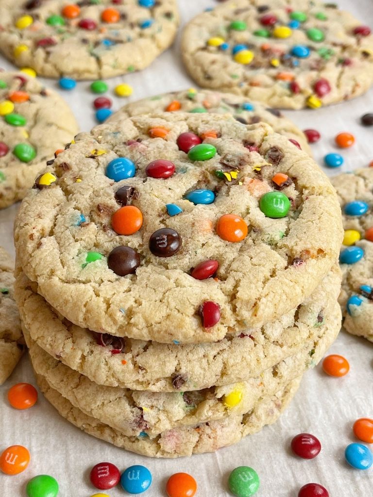 A stack of m&m cookies on a cookie sheet with mini m&m's around it.