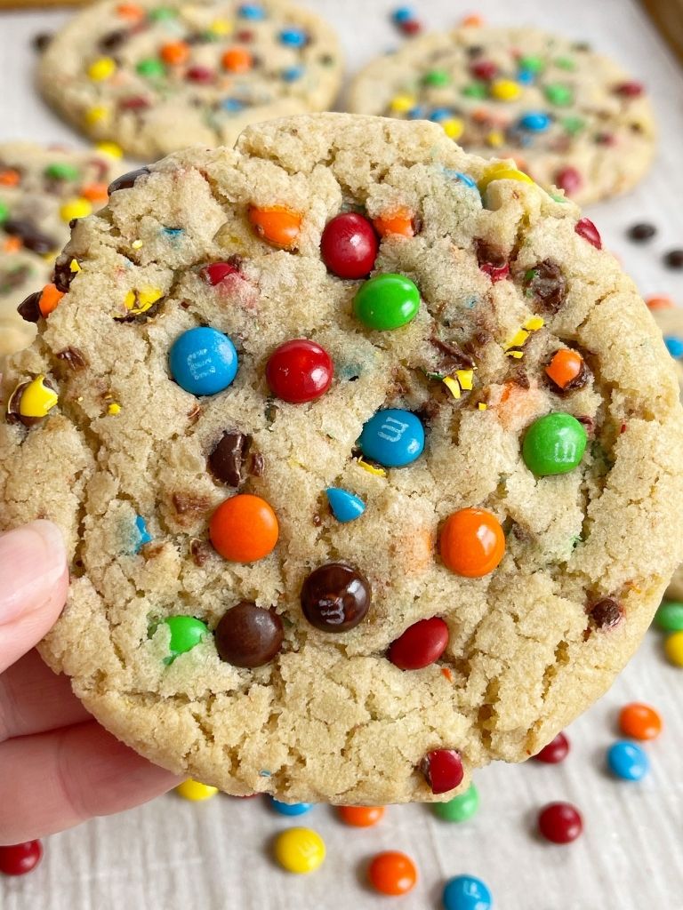 A hand holding a m&m cookie topped with mini m&m's on top.
