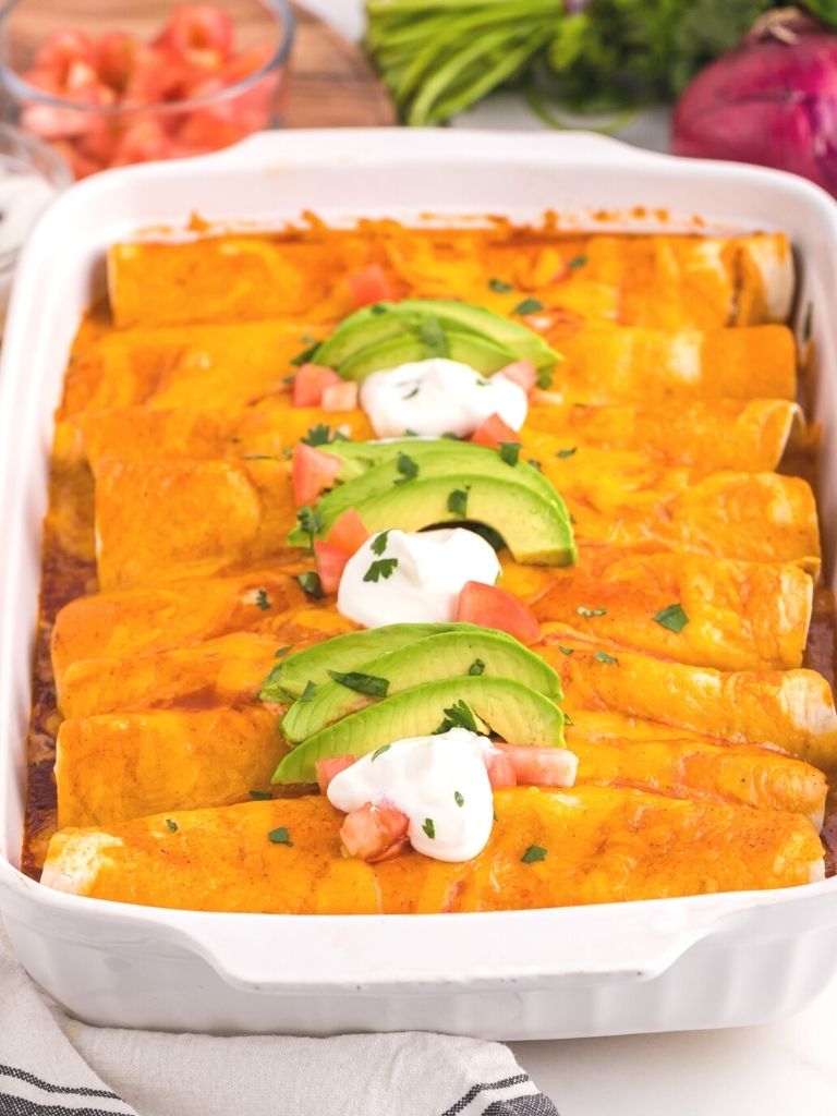 A white pan of enchiladas, baked, and topped with taco toppings. 