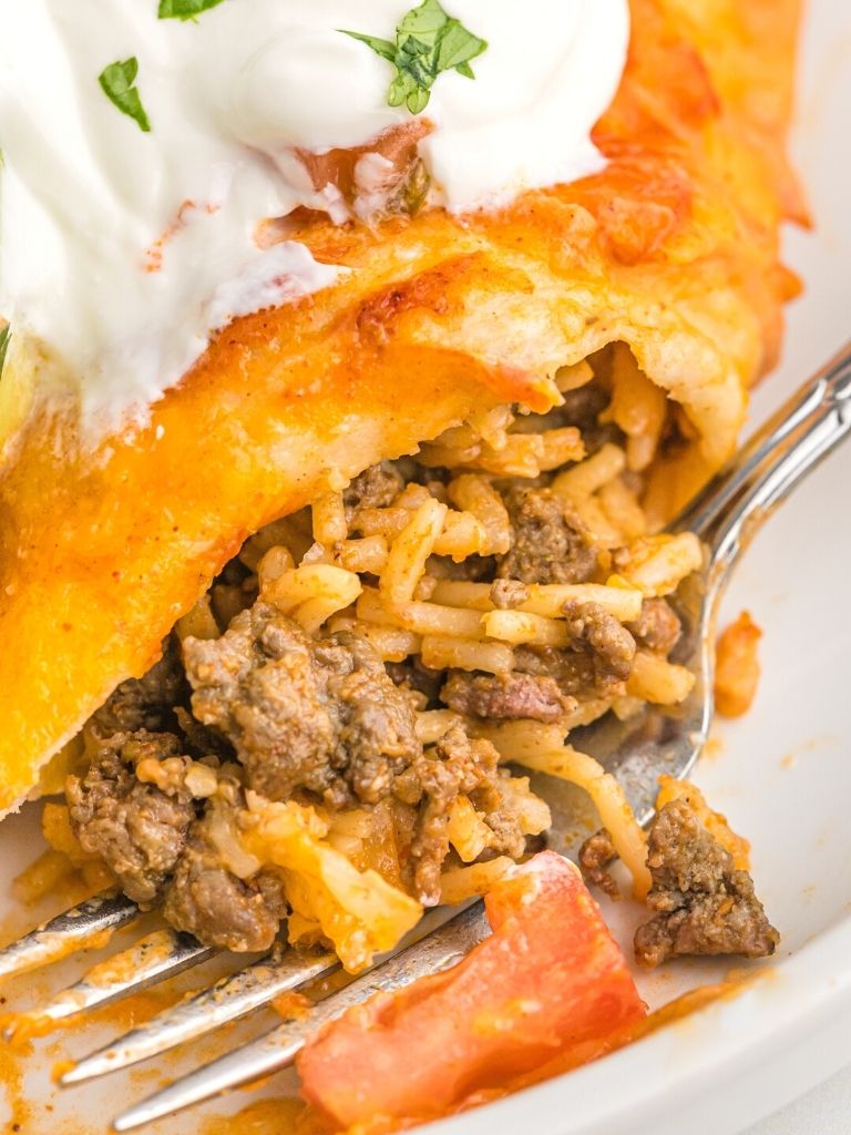A fork taking a bite out of an enchilada with ground beef. 
