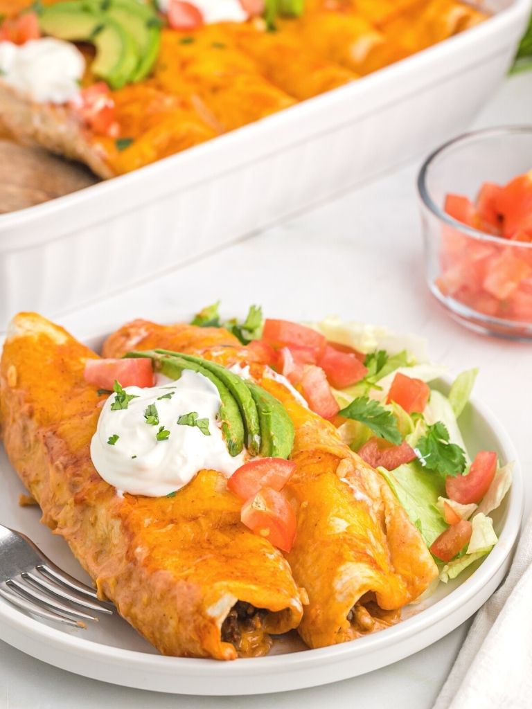 A plate with two enchiladas on it and a fork next to it. 