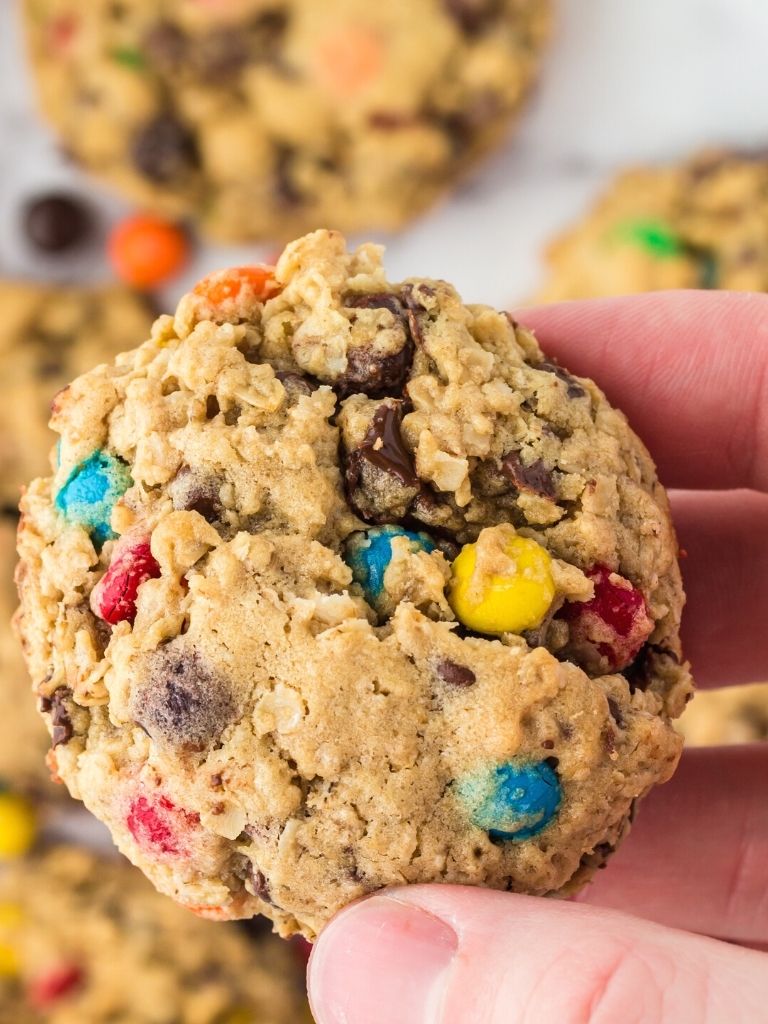 A hand holding one monster cookie in it with some cookies in the background.