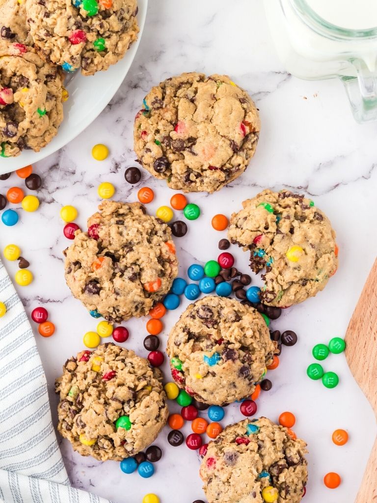 Overhead shot of monster cookies on a marble background with a glass of milk in the corner. 