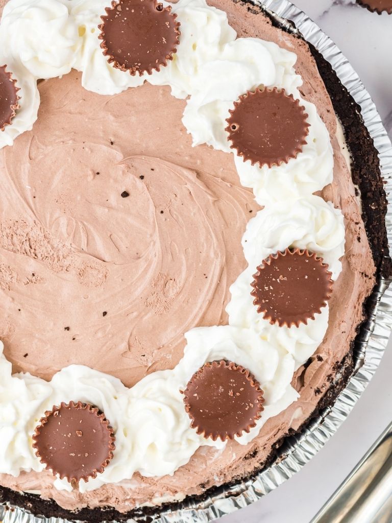 Overhead shot of a peanut butter pie garnished with peanut butter cups inside a foil tin. 