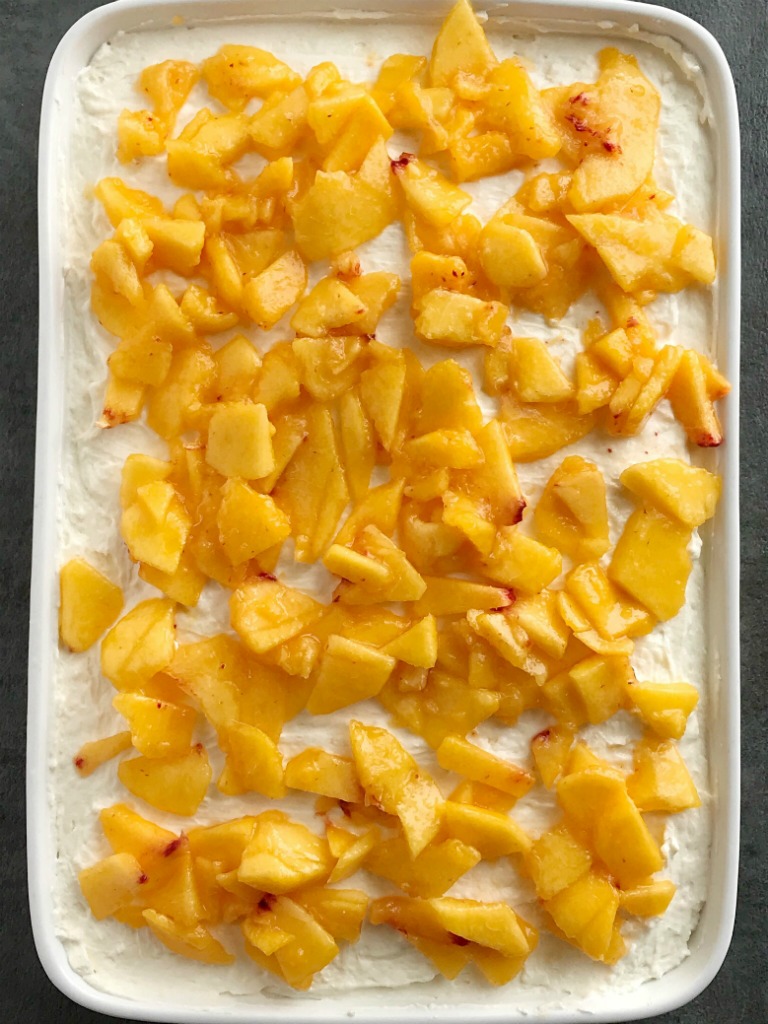 Peaches and Cream Poke Cake | Poke Cake Recipe | Cake | Dessert | If you love poke cakes then you must try this peaches and cream poke cake! French vanilla cake soaked in fresh peaches, frosted with a light and fluffy cream cheese whipped topping, and topped with chunked fresh peaches. #pokecake #cake #dessertrecipes #easydessertrecipe #peaches #peachrecipes