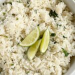 A white bowl of cilantro lime rice garnished with lime wedges on top.