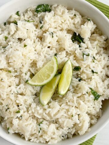 A white bowl of cilantro lime rice garnished with lime wedges on top.