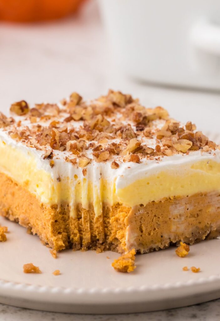 Front view of a slice of the pumpkin dessert with a fork bite taken out of the corner to show the layers. 