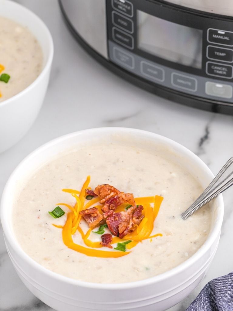 A bowl of soup with a slow cooker in the background.