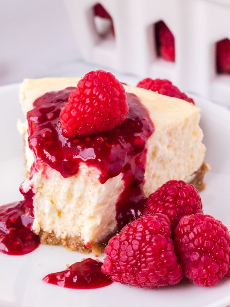 An image of a slice of cheesecake topped with raspberry sauce on a white plate with a bite taken out of the front of it. 