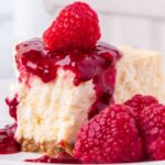 Slice of cheesecake with raspberry sauce and fresh raspberries on top.