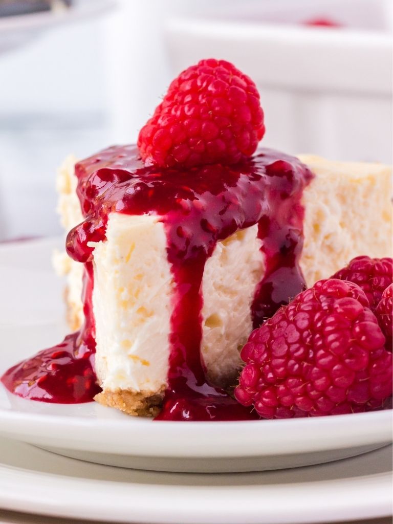Stacked white plates with a slice of cheesecake on top and topped with raspberry sauce.