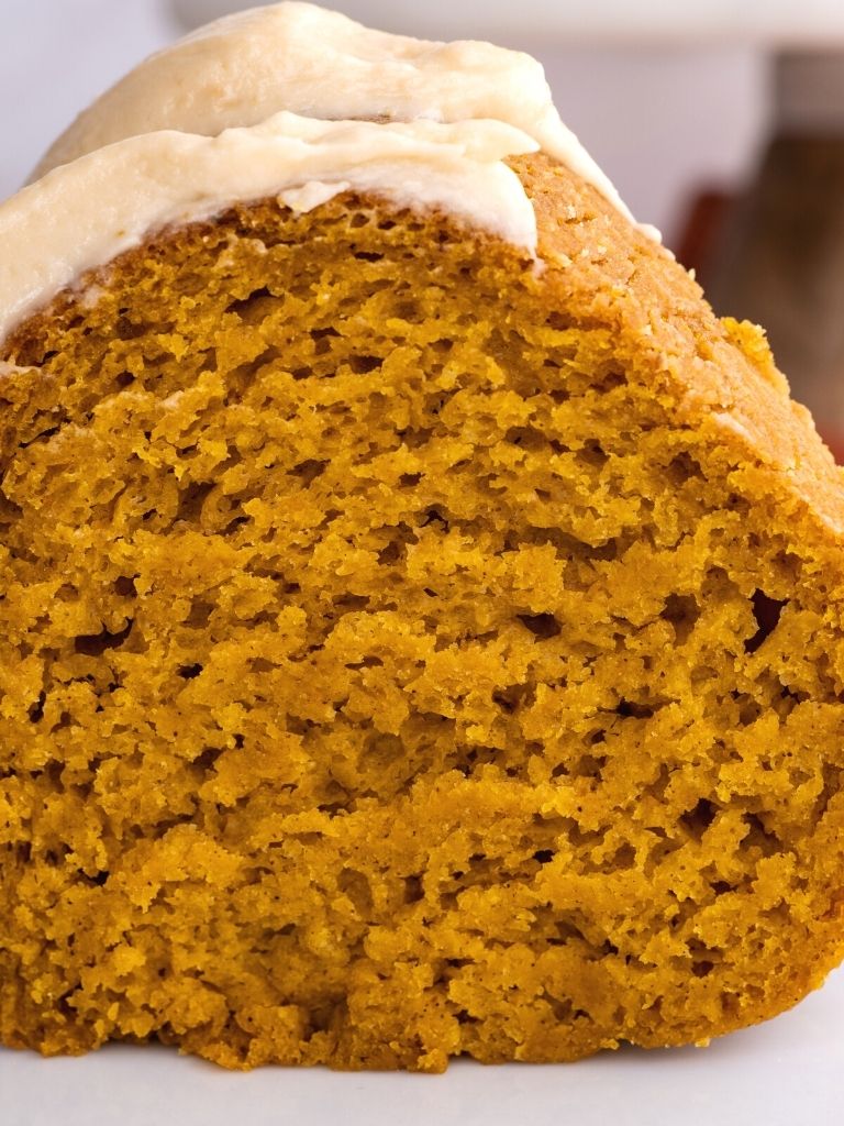 Picture of a slice of pumpkin bundt cake topped with caramel frosting on top of a white plate.