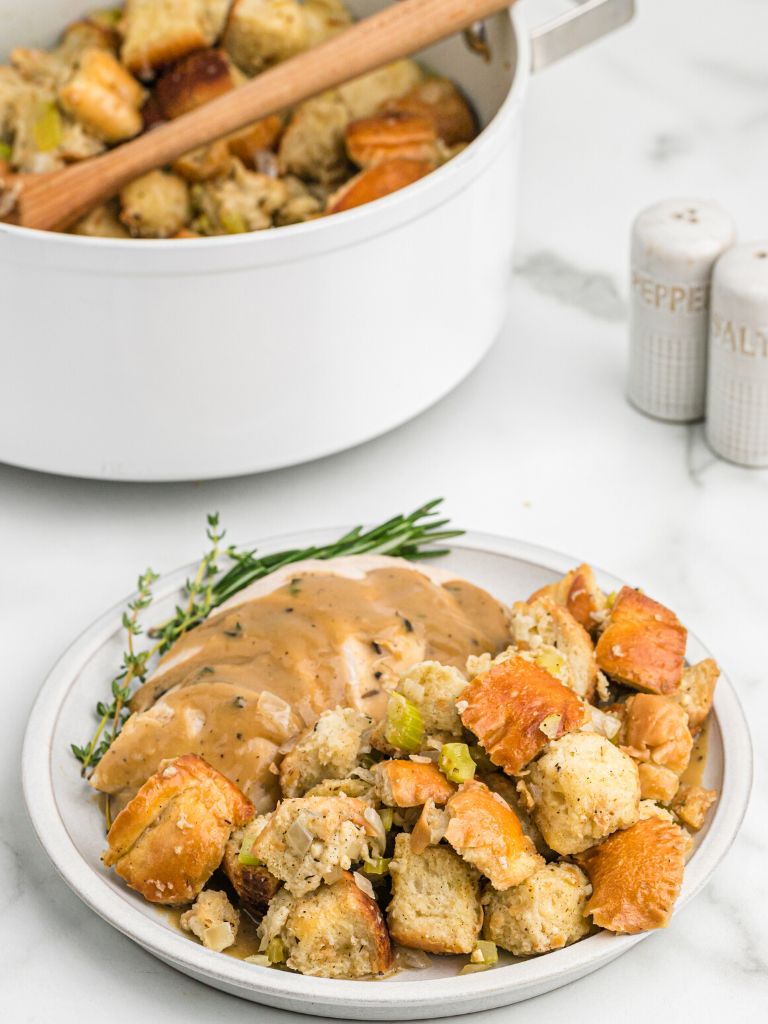 A plate setting with stuffing and turkey on it, with a pot of stuffing in the background. 