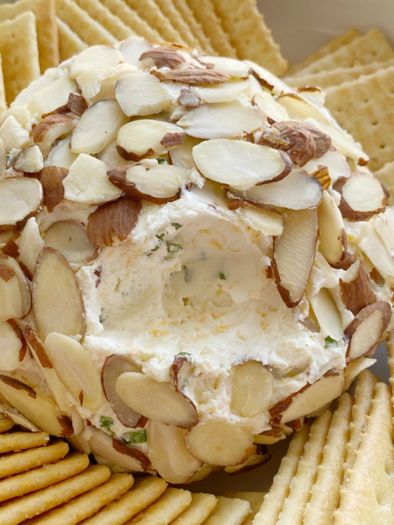 A cheeseball on a plate with crackers around it.