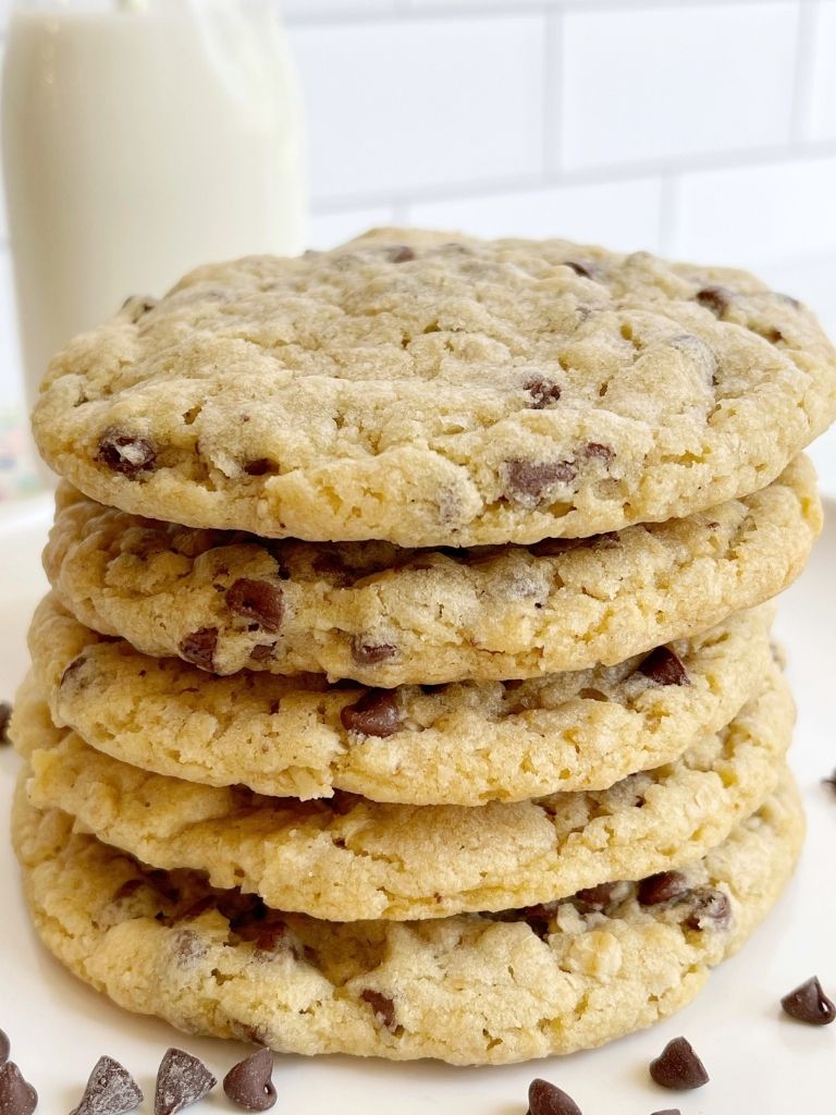 A stack of cookies on a white plate with a glass of milk behind them. 