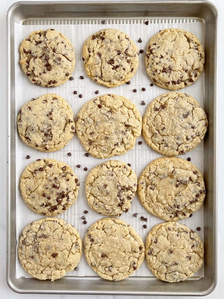 A cookie sheet with cookies on it and chocolate chips. 