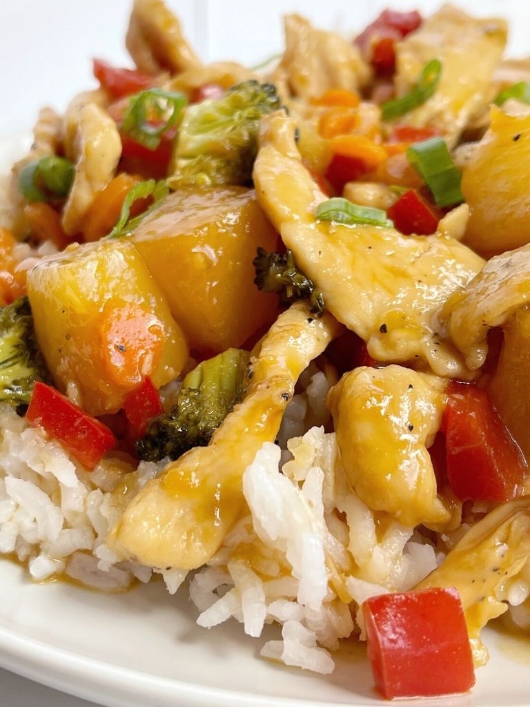 A plate with white rice and some chicken stir fry on top. 