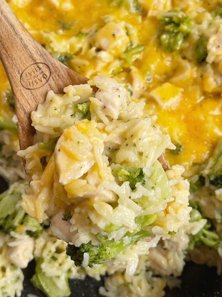 A wooden spoon with a scoop of cheesy chicken broccoli and rice.