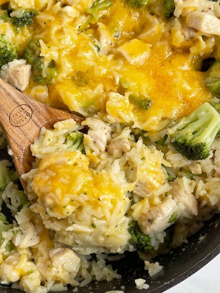 Skillet pan of cheesy rice and broccoli with a wooden spoon inside of it.