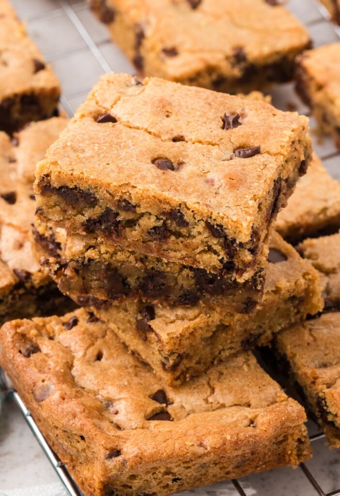 Stack of two blondie bars and some around it on the cooling rack of cookie bars. 