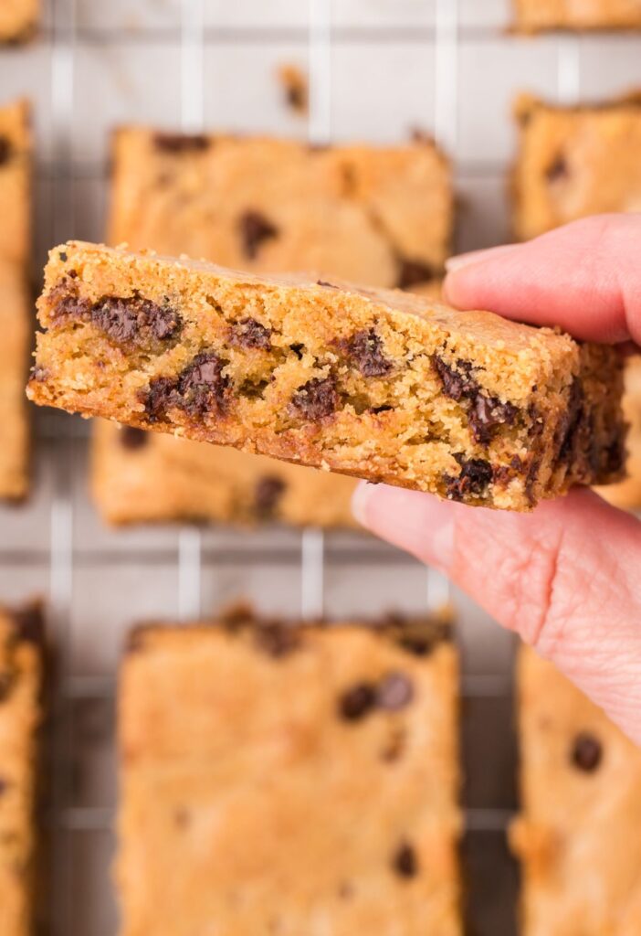 A hand holding a blondie bar cookie in its hand showing it up close. 