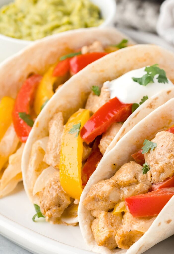Close up of chicken fajitas with bell peppers and sour cream. 