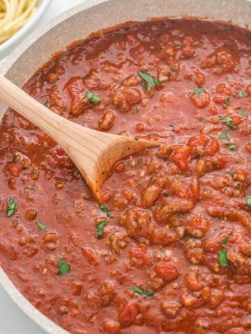 Picture of meat sauce inside a pan with a wooden spoon. Serve meat sauce over spaghetti noodles.