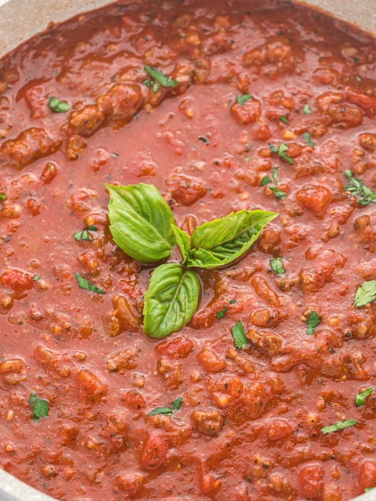 A pan of spaghetti meat sauce with a basil leaf in the center.