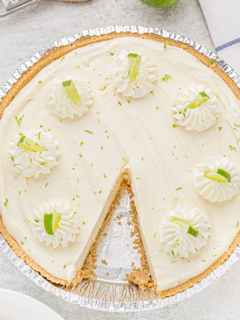 A pie with one slice cut out of it. Topped with lime zest and whipped cream. 