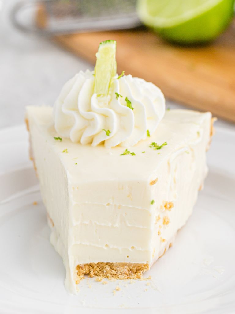 A slice of no bake pie topped with whipped cream and a lime slice. A bite taken out of the front.