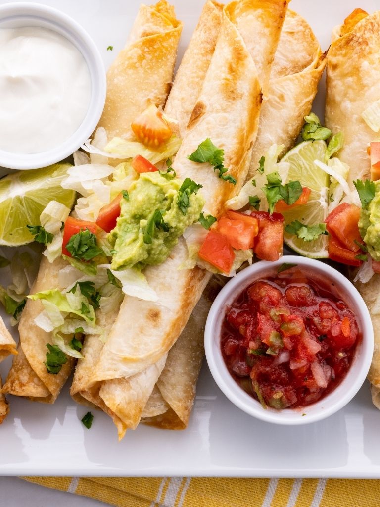Tray of flautas with a bowl of salsa and sour cream on the side. 