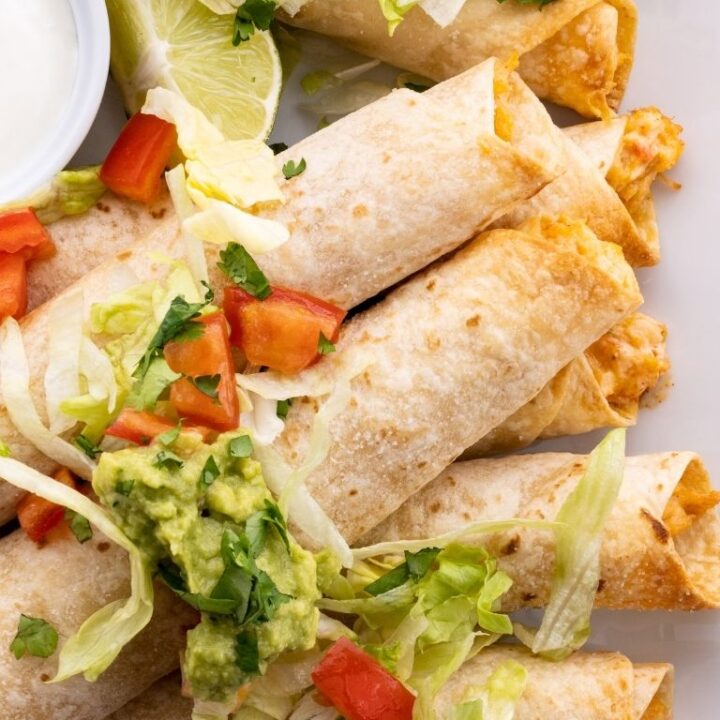 Chicken flautas on a white tray topped with lettuce, tomato, and guacamole.