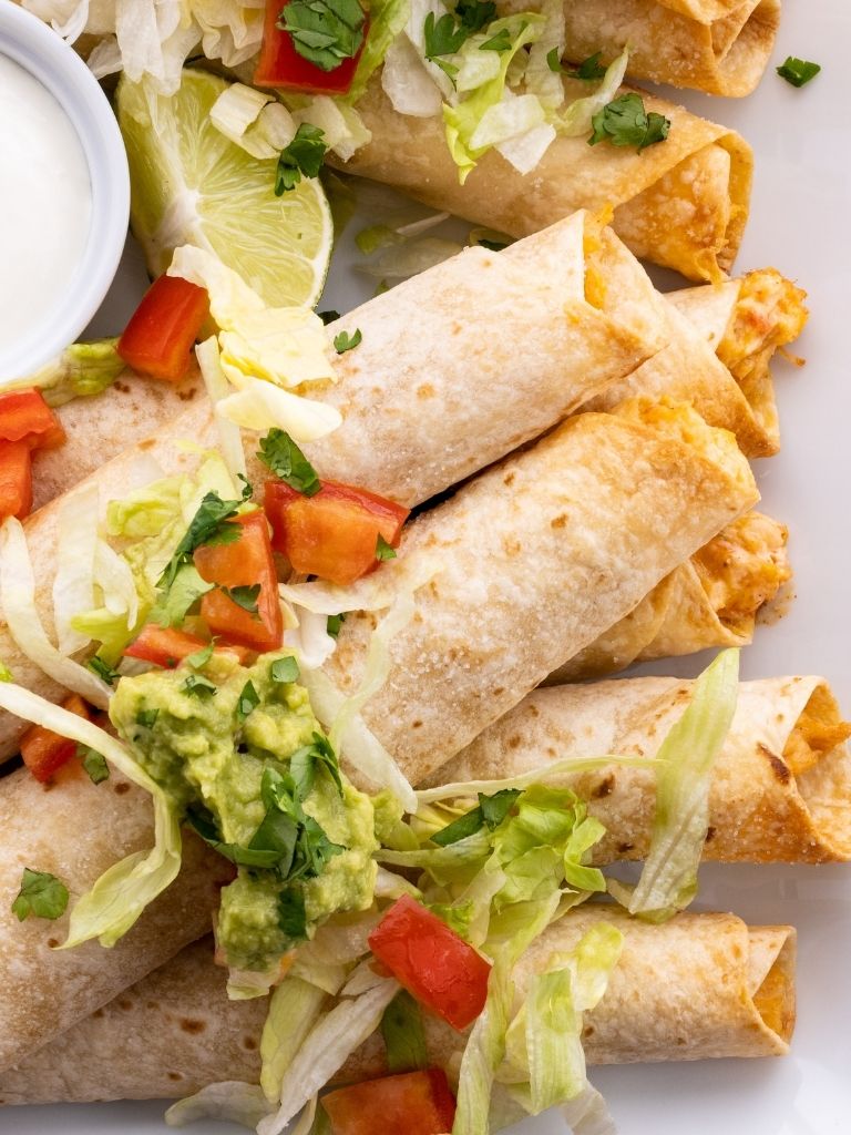 Chicken flautas on a white tray topped with lettuce, tomato, and guacamole. 