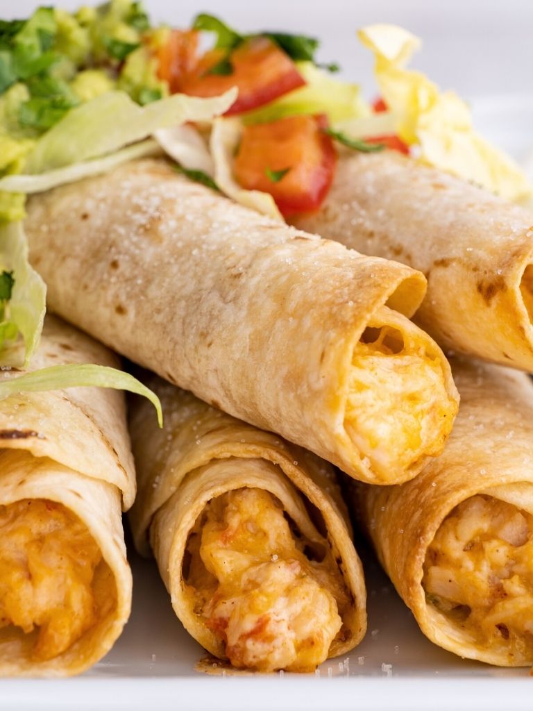 Close up shot of flautas on a white tray with cheese.