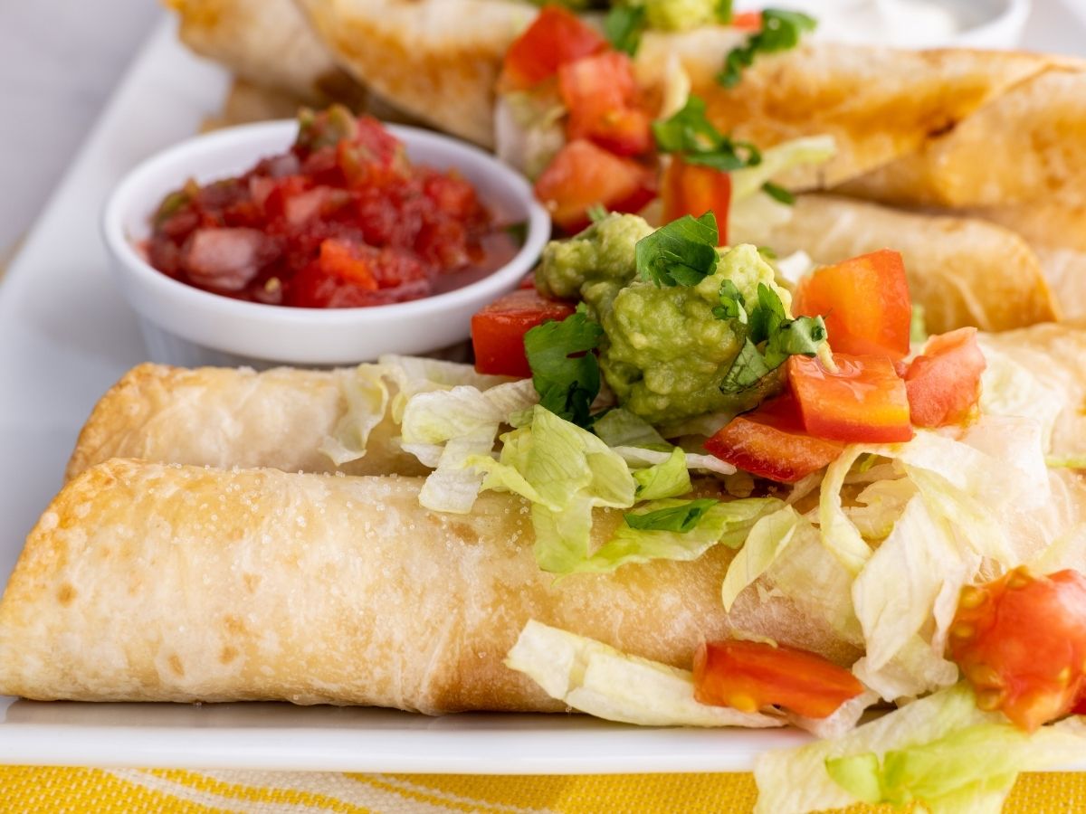 Horizontal picture of chicken flautas with a bowl of salsa. 