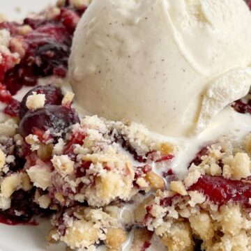 A picture of berry crisp dump cake on a white plate with a scoop of ice cream on top.