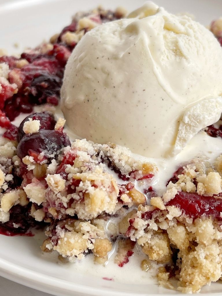 A picture of berry crisp dump cake on a white plate with a scoop of ice cream on top.