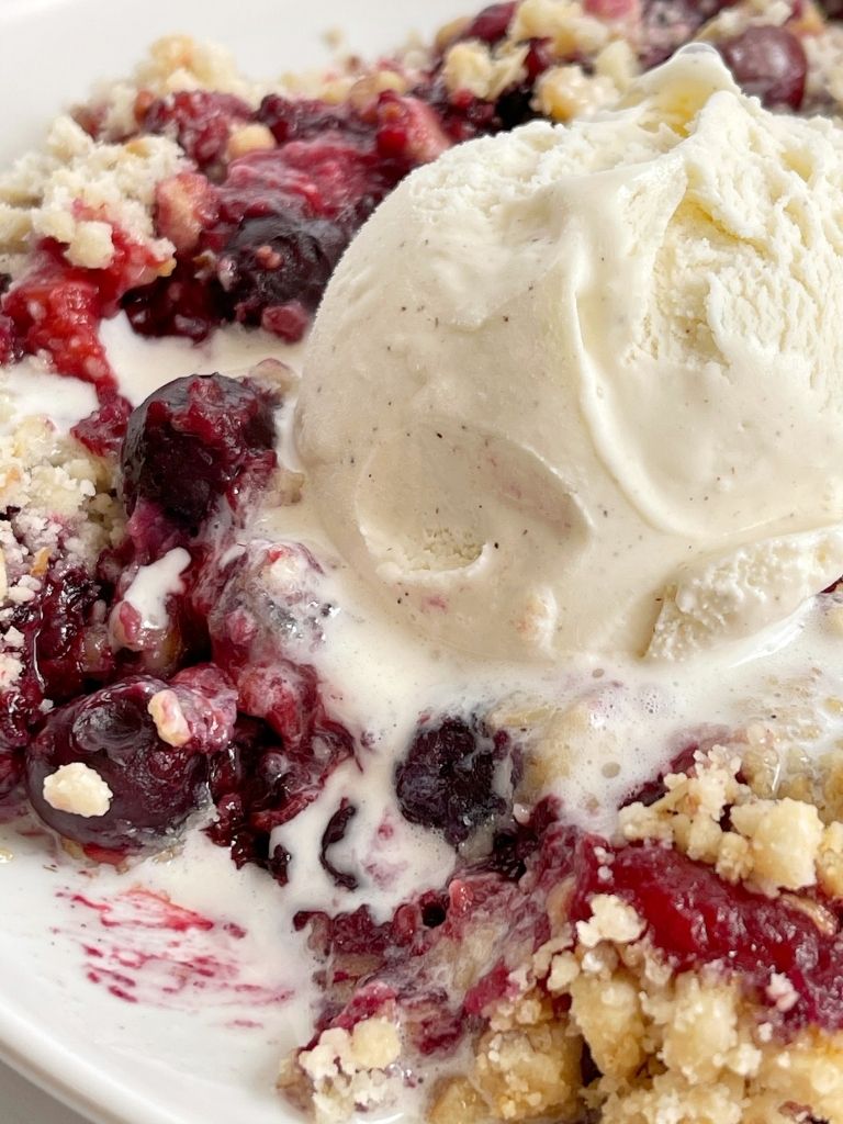 Plate of berry dump cake topped with a scoop of ice cream melting on top. 