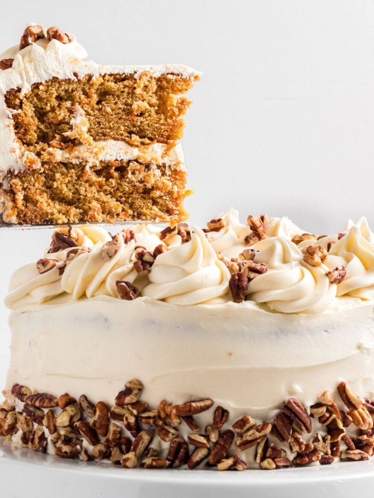Carrot cake with a slice on a spatula above the cake.