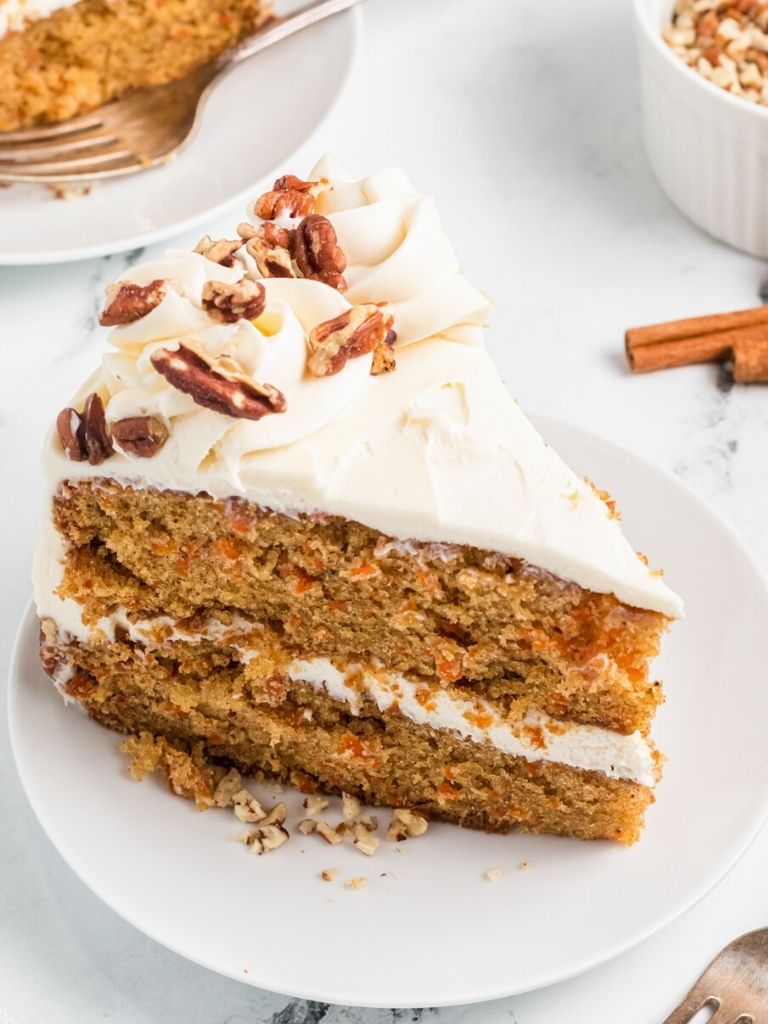 Slice of cake on a white plate garnished with frosting and pecans.