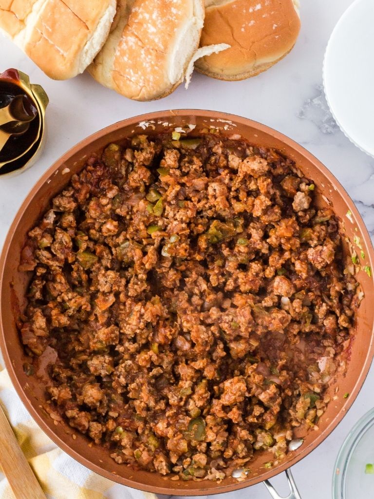 A pan of sloppy Joe mixture with rolls in the background. 