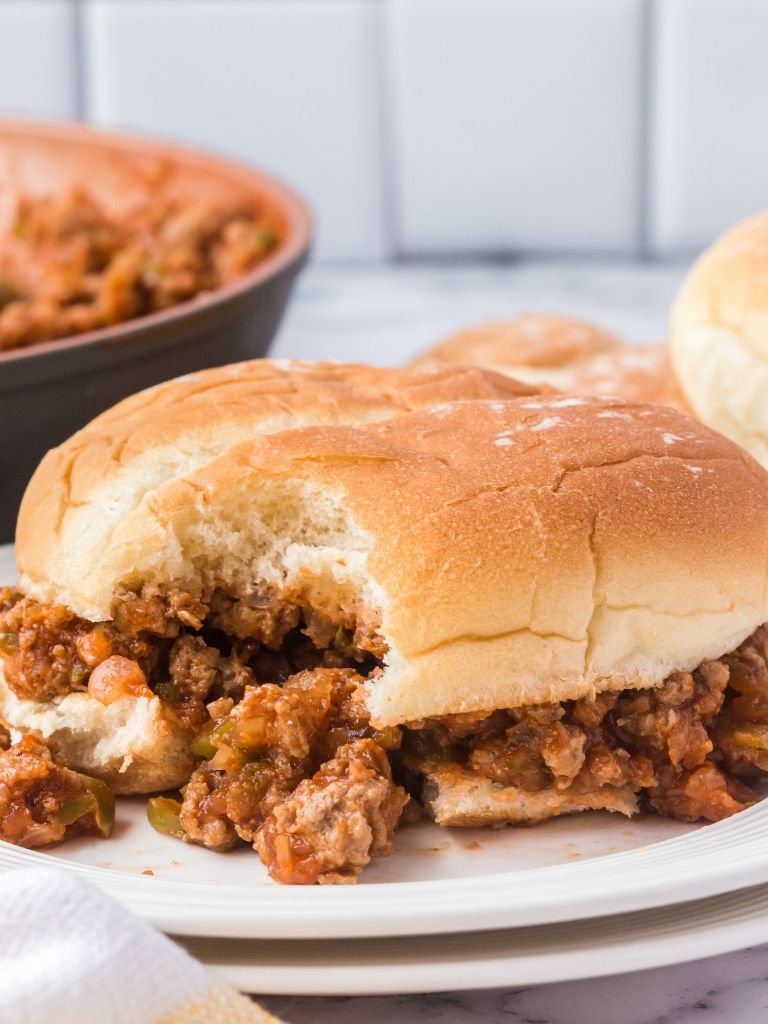 Sloppy Joes on a white plate with a bite taken out of it. 