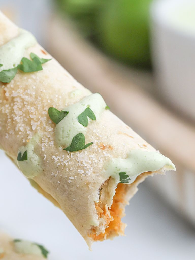 A taquito with a bite taken out of it and cilantro and sauce, salt on top of the tortilla. 