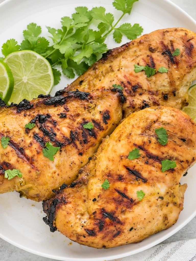 A plate of grilled chicken breasts with lime and cilantro garnishing the white plate.