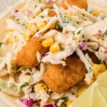 A corn tortilla with fish sticks and a cabbage slaw on it.