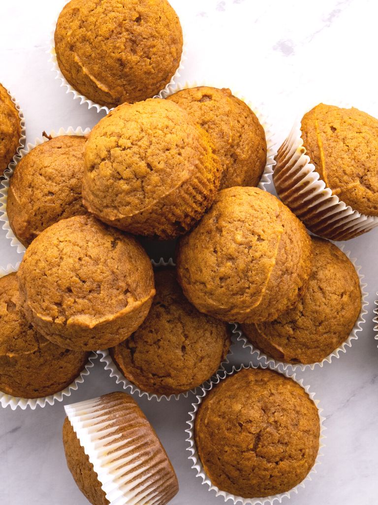 A stack and pile of muffins inside muffin liners. 