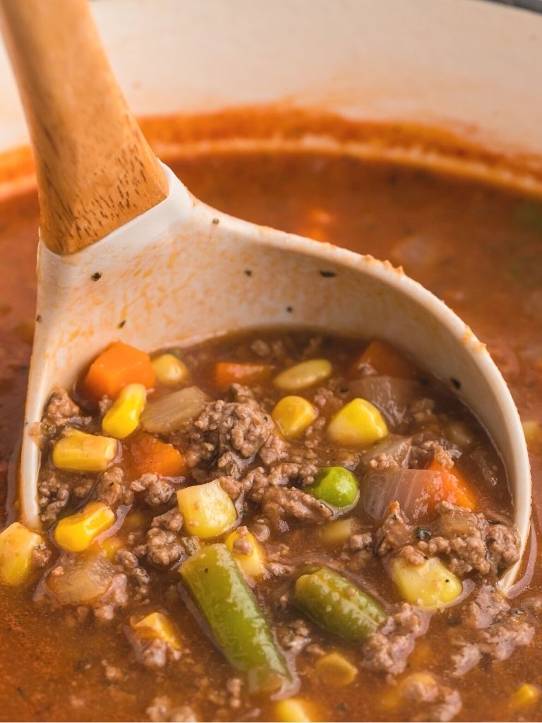 Ground beef soup inside a ladle in a soup pot full of soup.